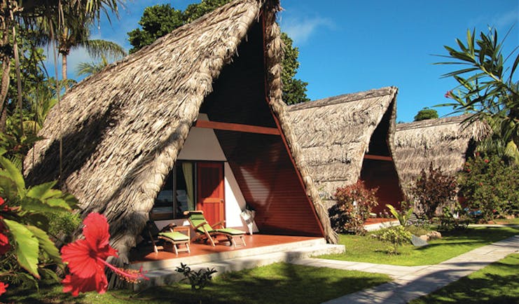 La Digue Island Lodge chalet exterior, triangle shped building, thatched roof, pathway across green lawn to front door