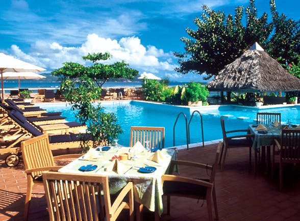 Pool restaurant with tables and chairs set up around the pool edge and sunloungers nearby