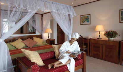 Domaine de la Reserve Seychelles bedroom relaxation woman relaxing on ottoman in front of four poster bed