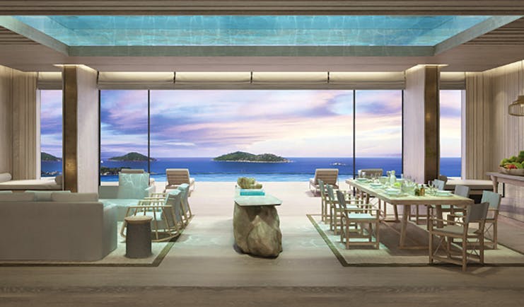 Six Senses Zil Pasyon residence lounge, modern decor, large dining table and sofa, glass walls with views across the ocean to adjacent islands