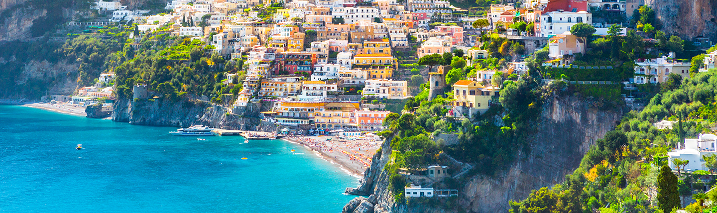 Many white and coloured houses on hillside leading to beach and sea with cliffs behind