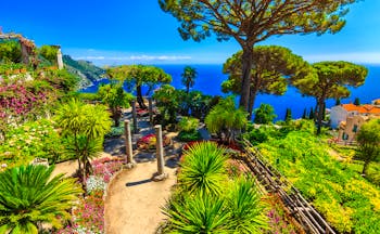 Palms and umbrella pine trees in ornamental garden at Villa Rufolo overlooking deep blue sea