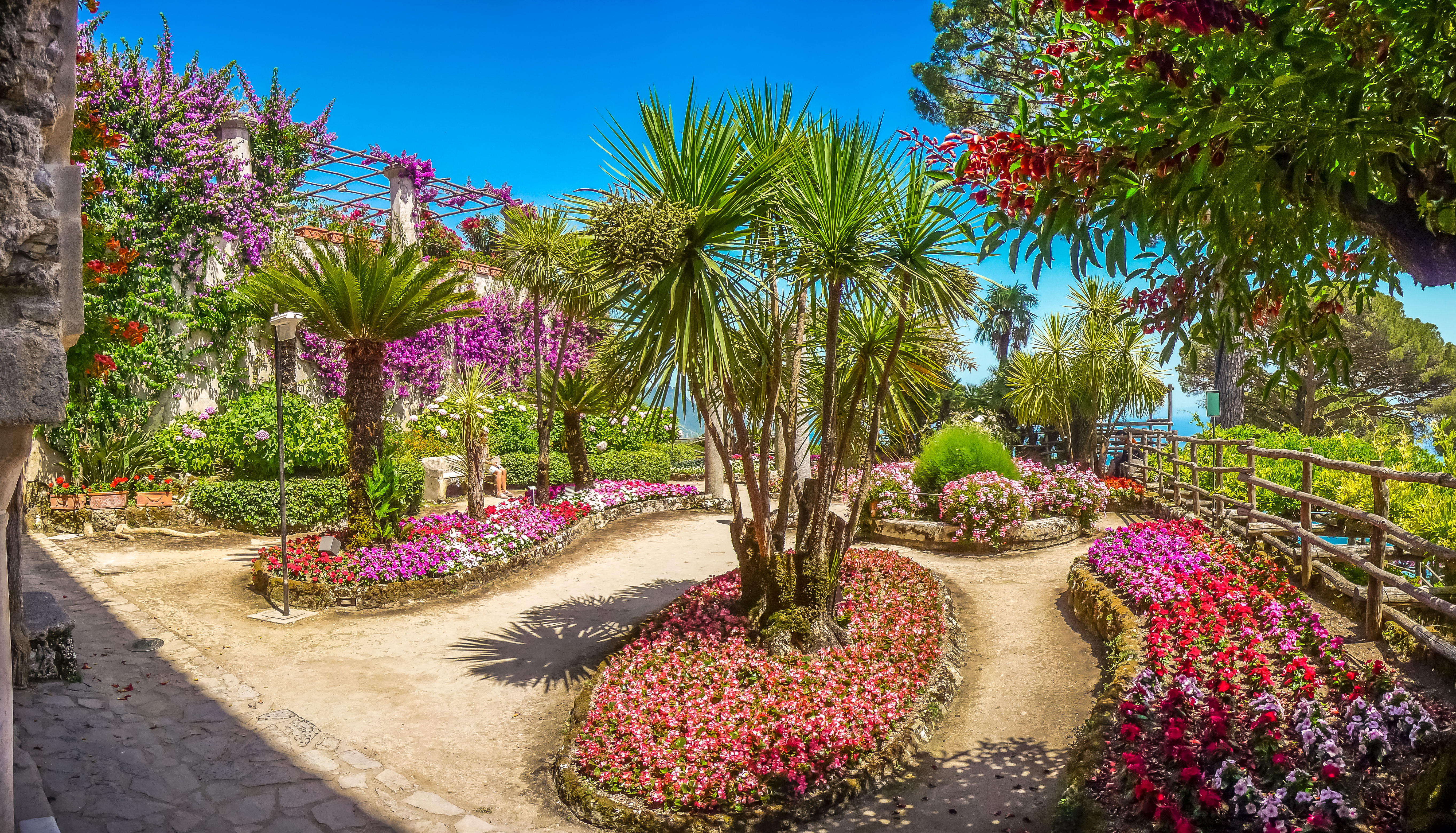 Beds of pink and red flowers and palm trees in the villa rufolo in Ravello