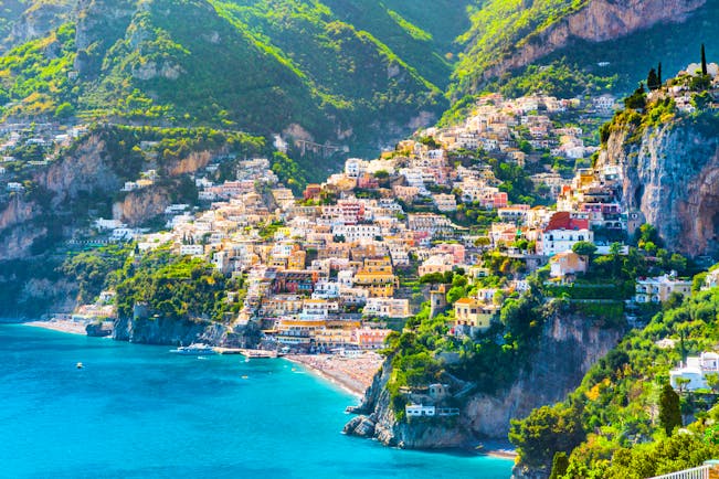 Distant view of Positano across turquoise sea with rows of houses lining hillside