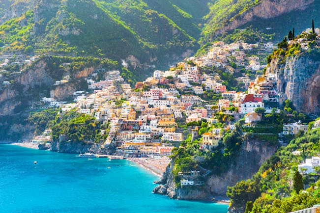 Distant view of Positano across turquoise sea with rows of houses lining hillside