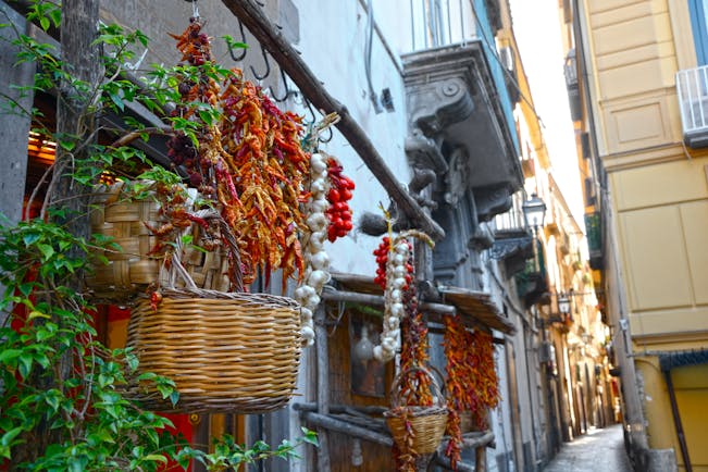 Narrow street lined with baskets and strings of garlic, dried chillies and tomatoes in Sorrento