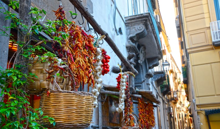 Narrow street lined with baskets and strings of garlic, dried chillies and tomatoes in Sorrento