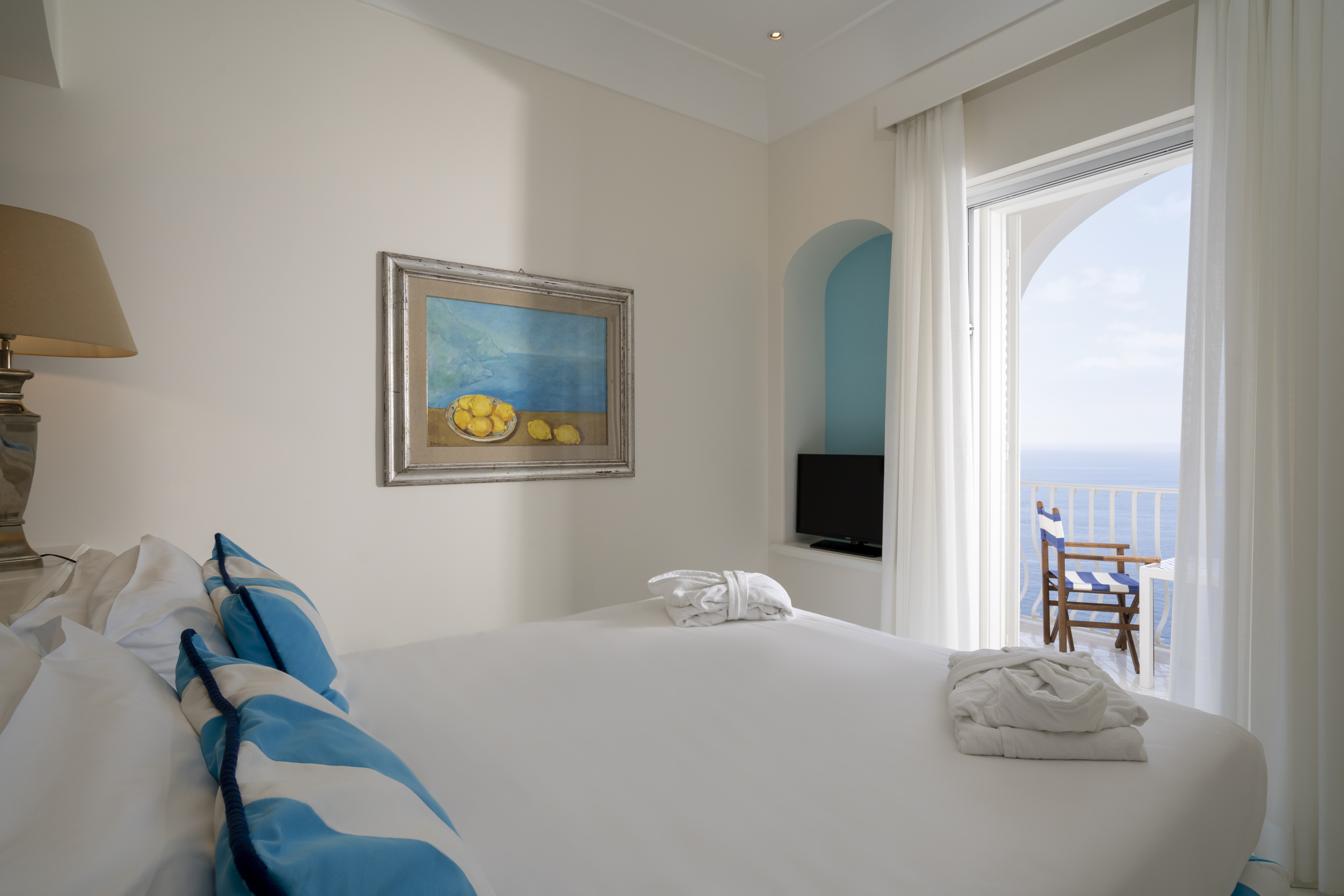 Hotel Tramonto d'Oro guestroom with white decor and bright blue accents, with doors opening onto a sea view balcony