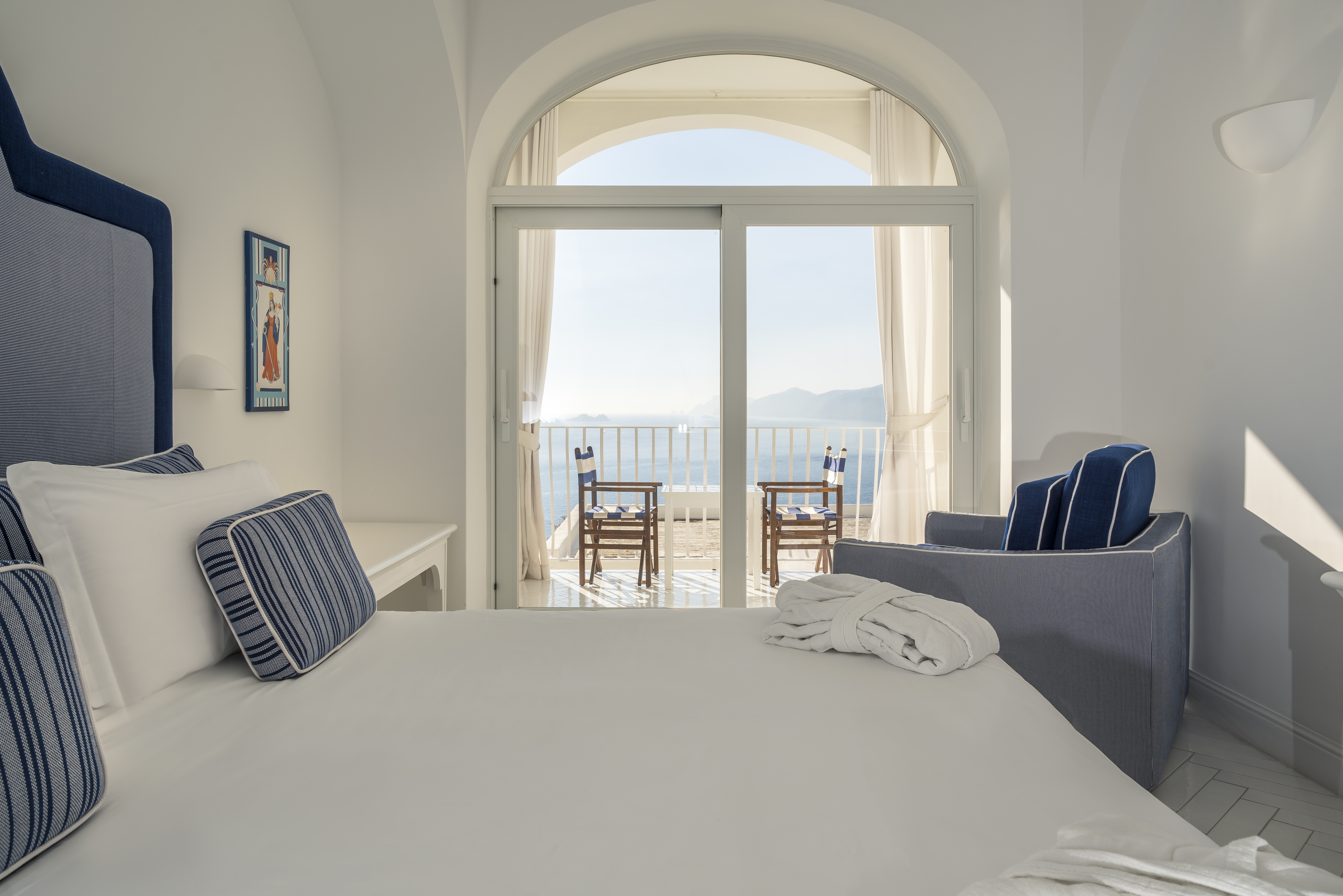 Hotel Tramonto d'Oro guestroom with white and navy blue decor and double arched doors leading onto a seaview balcony