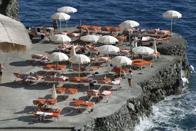 View of the hotel's beach, with red sunbeds and white umbrellas scattered around on the black rocky coast