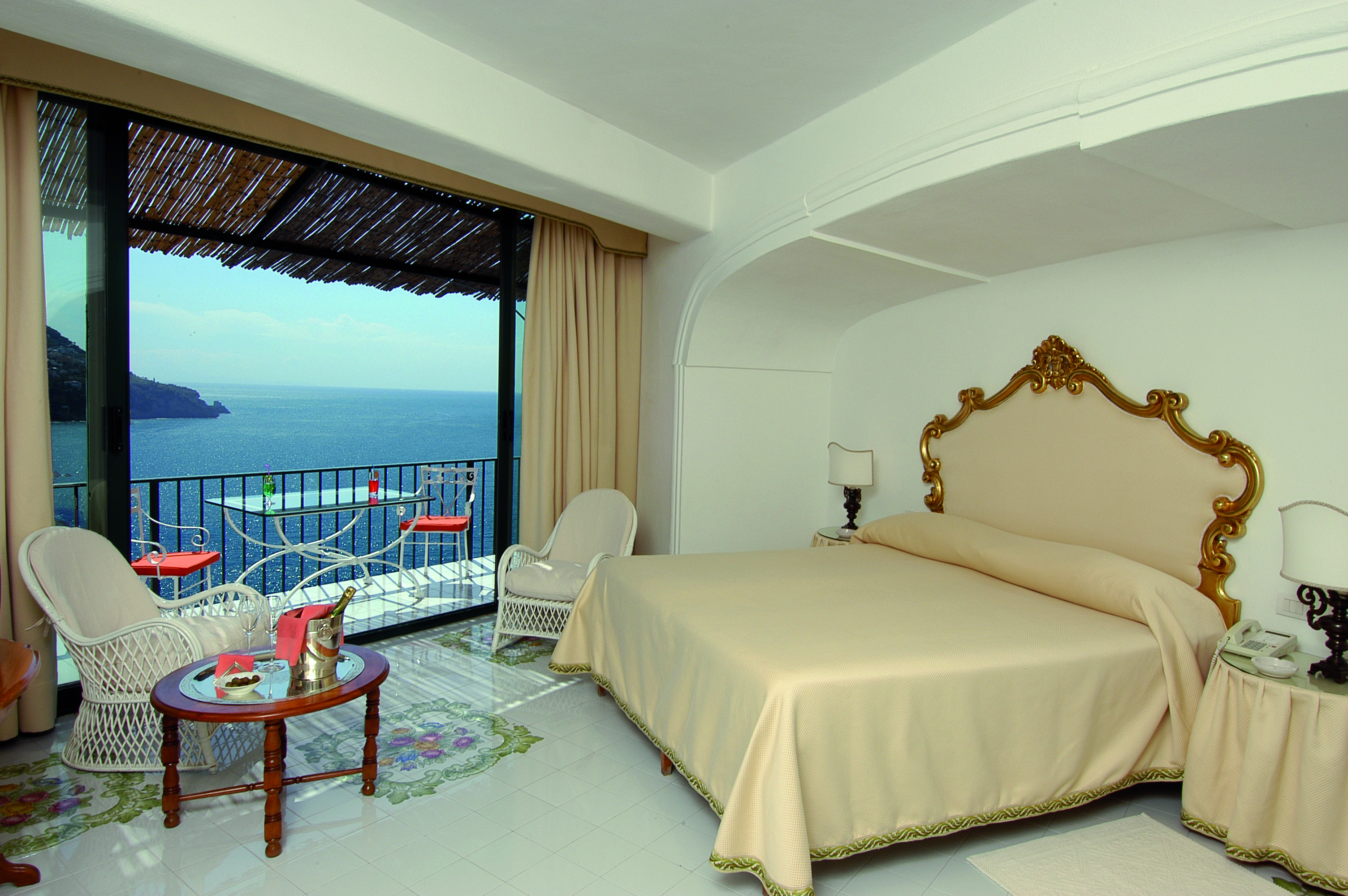 Bedroom at the Il San Pietro di Positano with cream and gold colourings, a large double bed and doors opening up onto a balcony overlooking the sea 