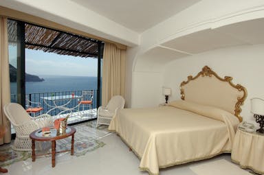 Bedroom at the Il San Pietro di Positano with cream and gold colourings, a large double bed and doors opening up onto a balcony overlooking the sea 