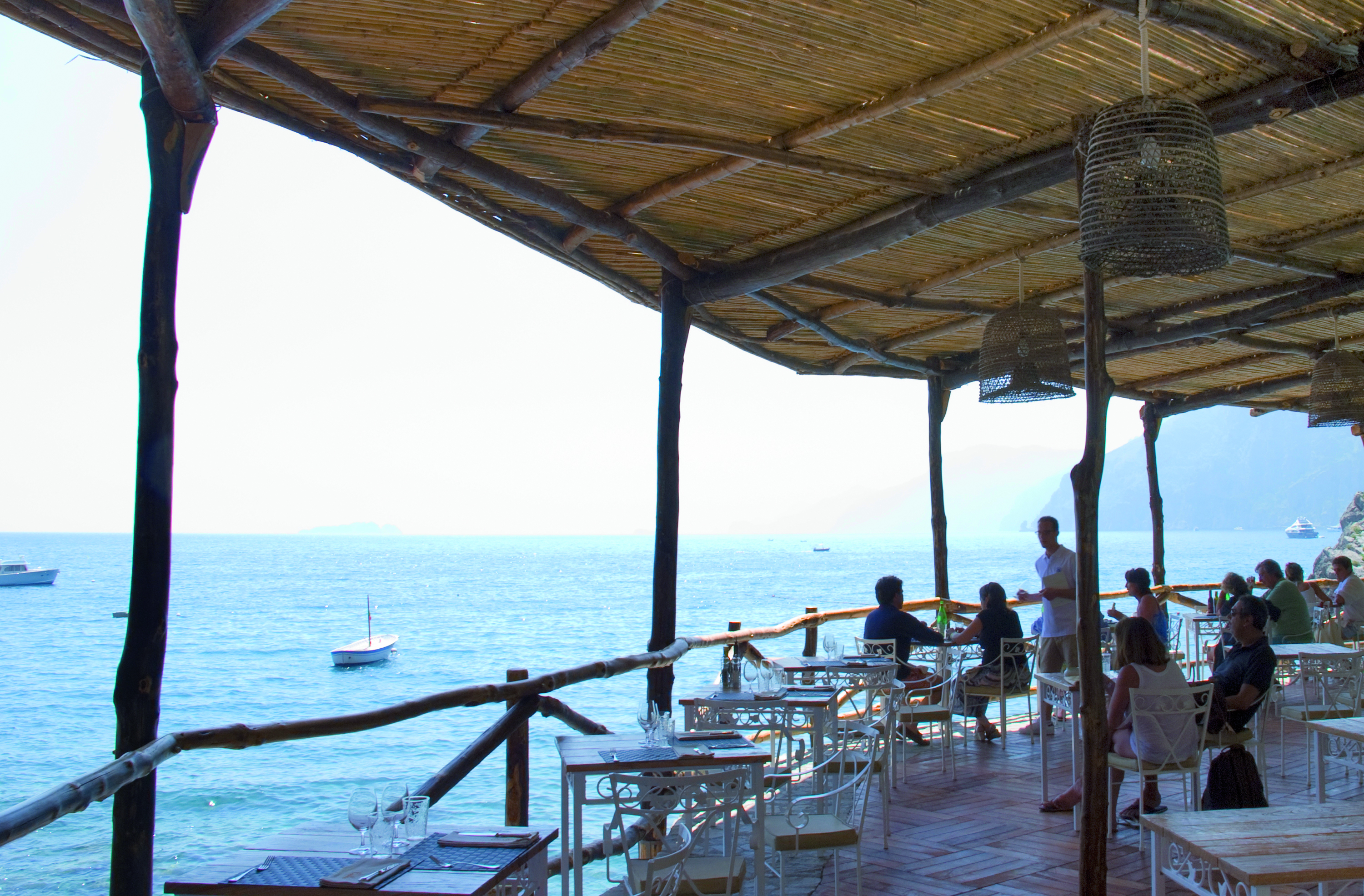 View of the Carlino restaurant looking over the sea, with a beach hut style roof and white table and chairs