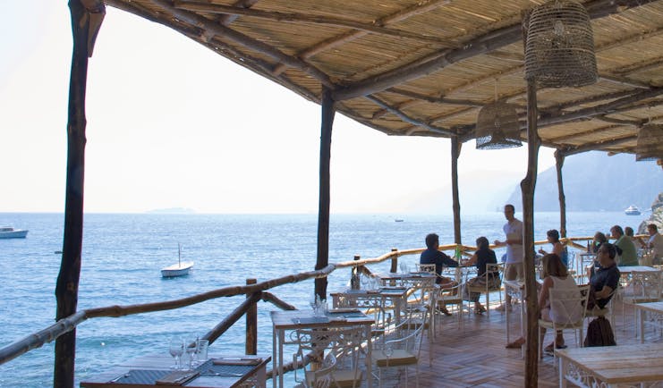 View of the Carlino restaurant looking over the sea, with a beach hut style roof and white table and chairs