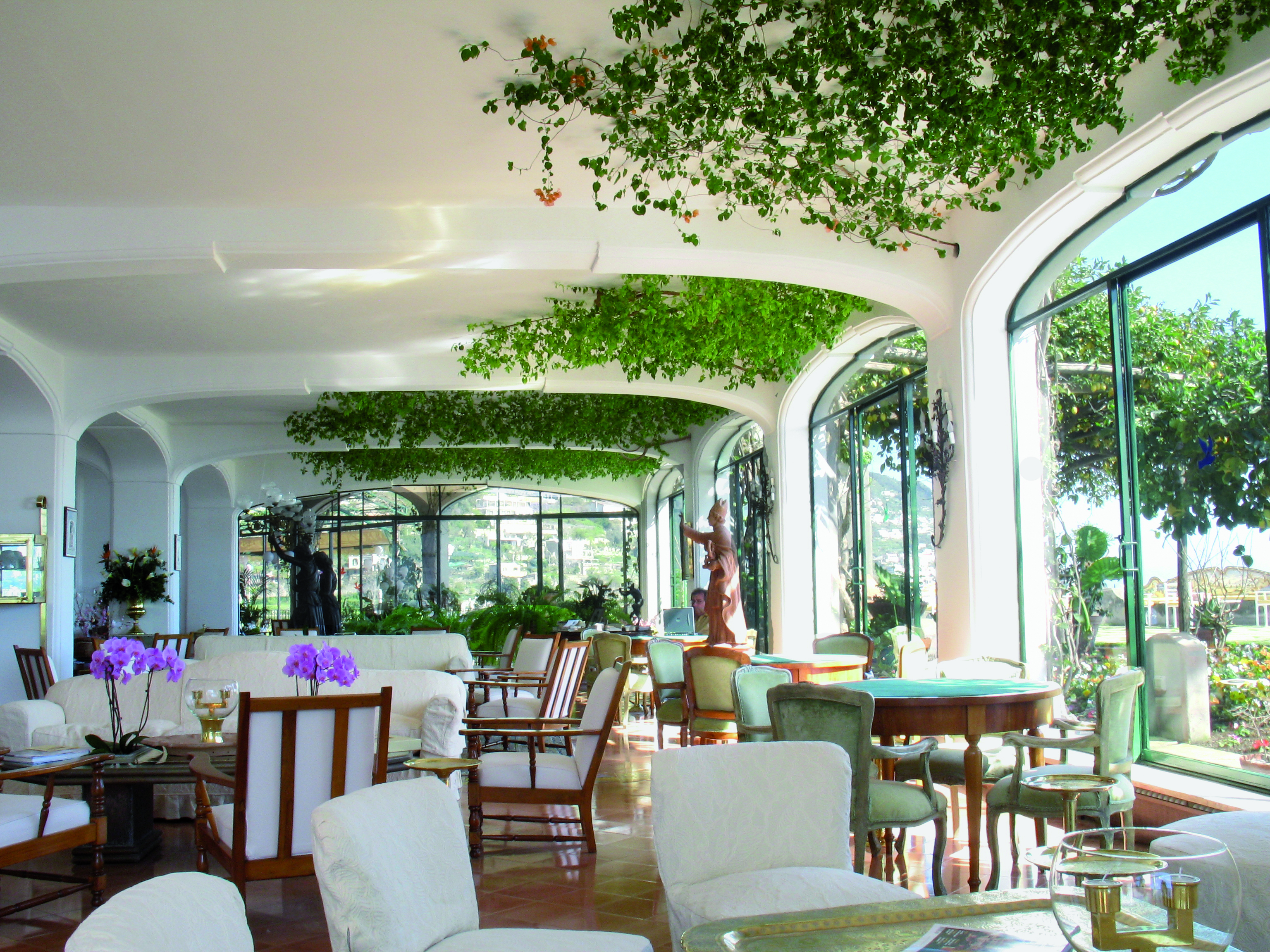 Il San Pietro di Positano lobby seating area with white and wooden, plants scattered around the room and large windows looking out onto the scenery