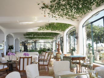Il San Pietro di Positano lobby seating area with white and wooden, plants scattered around the room and large windows looking out onto the scenery