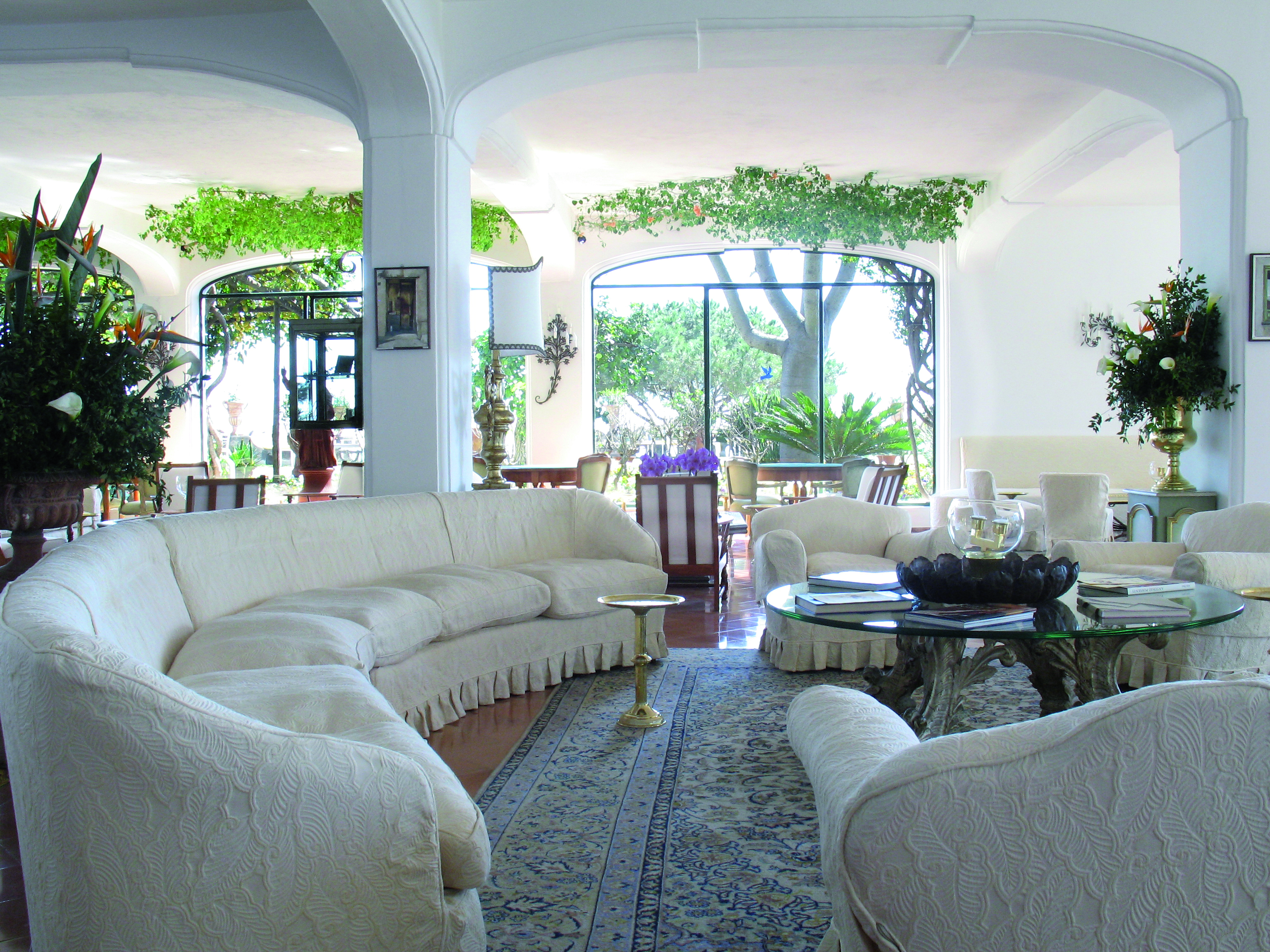Lobby at the Il San Pietro di Positano with a long curving white sofa, big windows looking out onto the gardens and a cream colour scheme