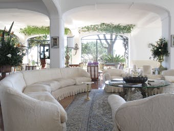 Lobby at the Il San Pietro di Positano with a long curving white sofa, big windows looking out onto the gardens and a cream colour scheme