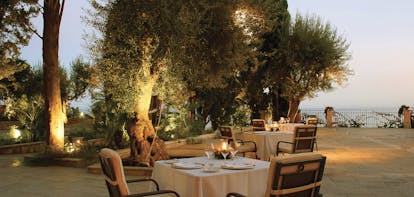 Outdoors restaurant at the Il San Pietro di Positano with palm trees in the background and lights in the trees. A four person table is set 