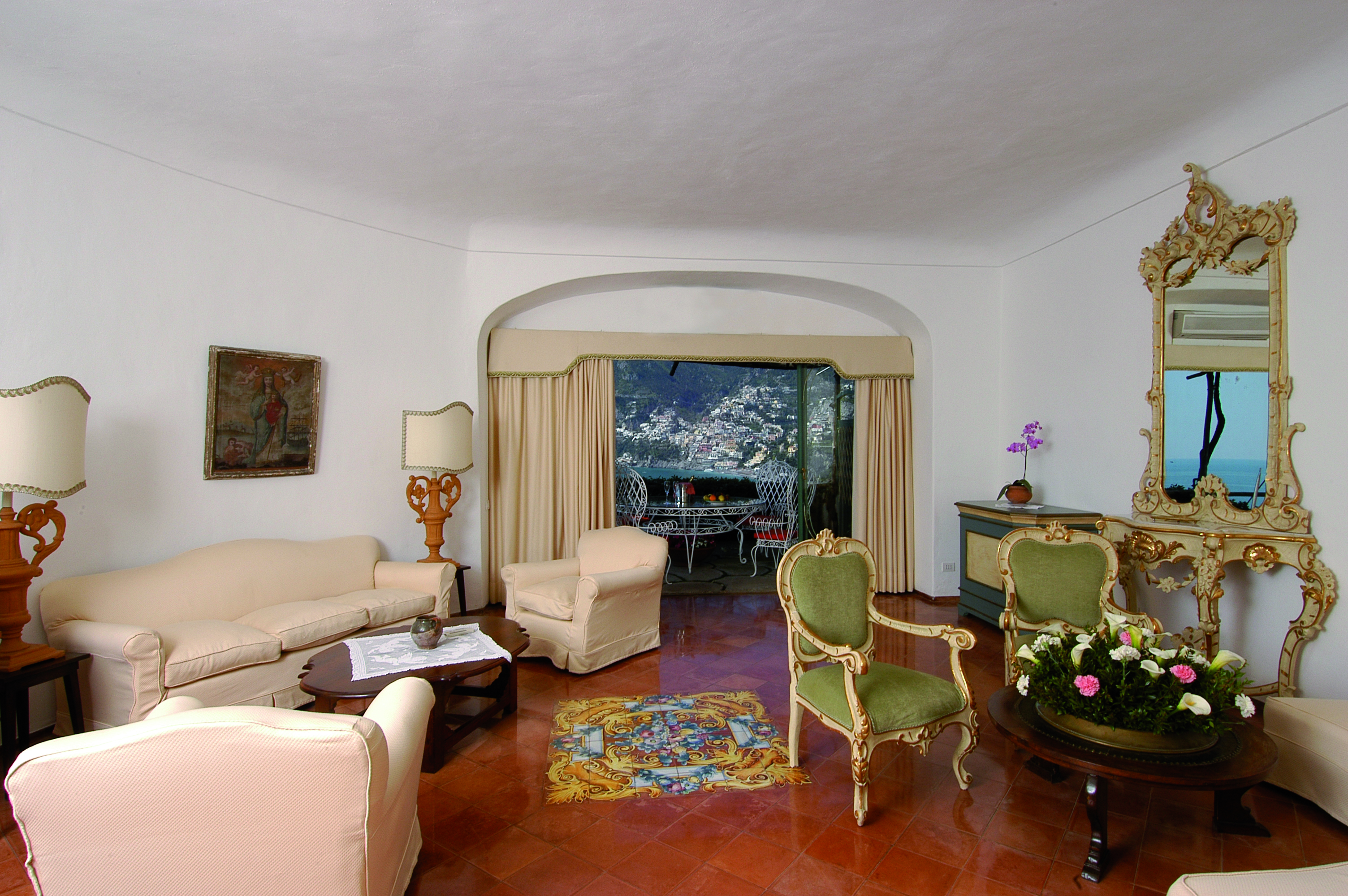 View of a suite living room in the Il San Pietro di Positano with cream sofas, green chairs and large windows leading onto a balcony