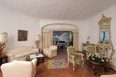 View of a suite living room in the Il San Pietro di Positano with cream sofas, green chairs and large windows leading onto a balcony