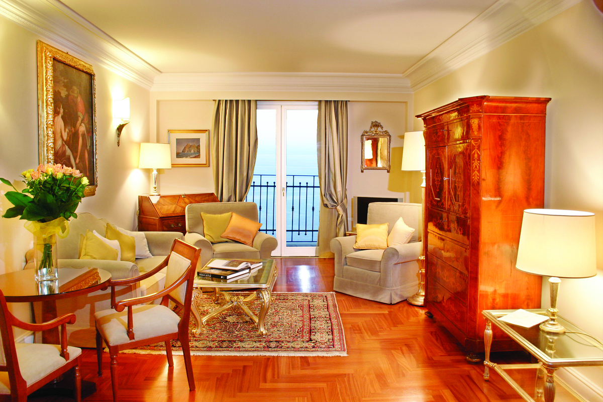 Suite at the Il San Pietro di Positano with a dining table, closet and double doors leading out onto a balcony, overlooking the sea