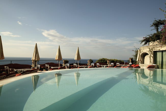 View of the Il San Pietro di Positano clear blue swimming pool with white umbrellas around the pool 