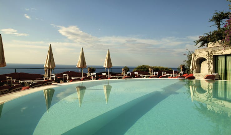 View of the Il San Pietro di Positano clear blue swimming pool with white umbrellas around the pool 