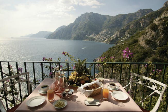 View from the balcony of a terrace suite with a breakfast display laid out on a table, looking over the sea and mountain regions 