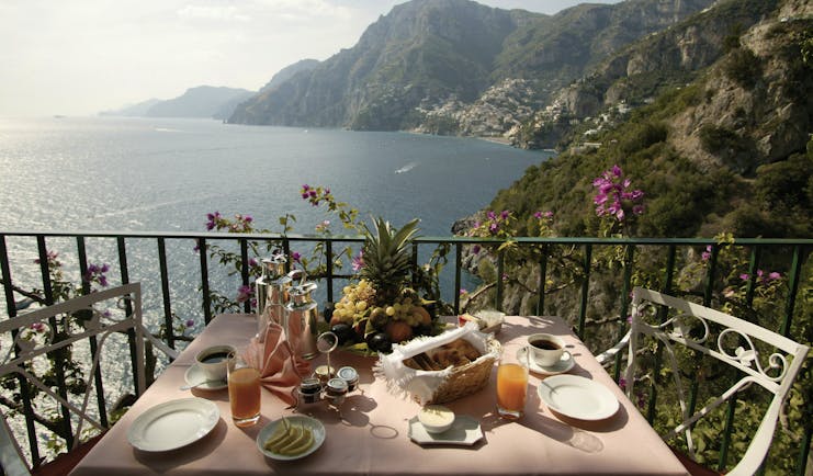 View from the balcony of a terrace suite with a breakfast display laid out on a table, looking over the sea and mountain regions 