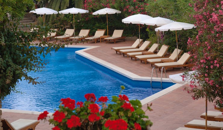 Outdoor pool with sun loungers and umbrellas around the edge of the pool and red flowers around