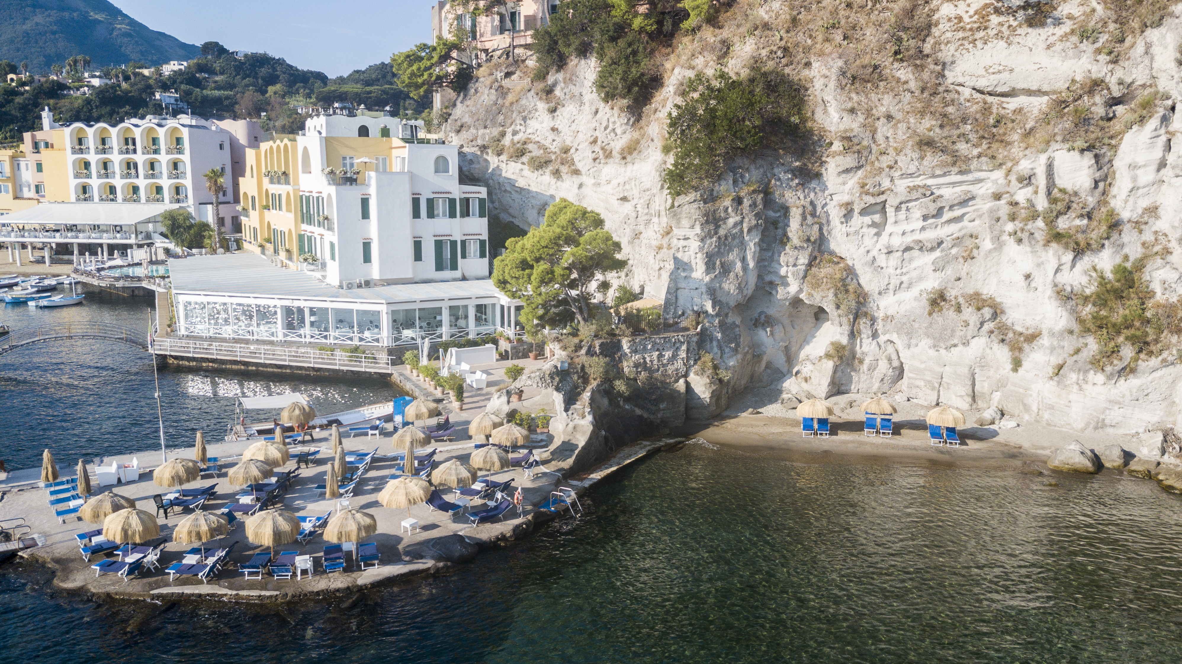 Regina Isabella beach club, manmade structure over the sea with sun loungers and umbrellas, small cove, hotel building in background