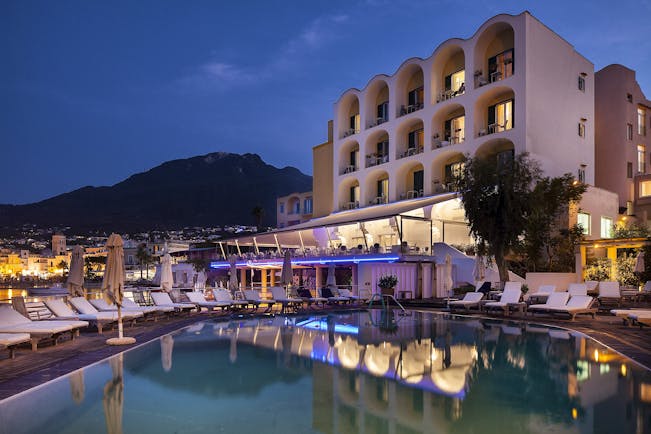 Regina Isabella exterior at dusk, hotel building, pool, sun loungers, town and moutains in background