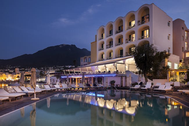 Regina Isabella exterior at dusk, hotel building, pool, sun loungers, town and moutains in background