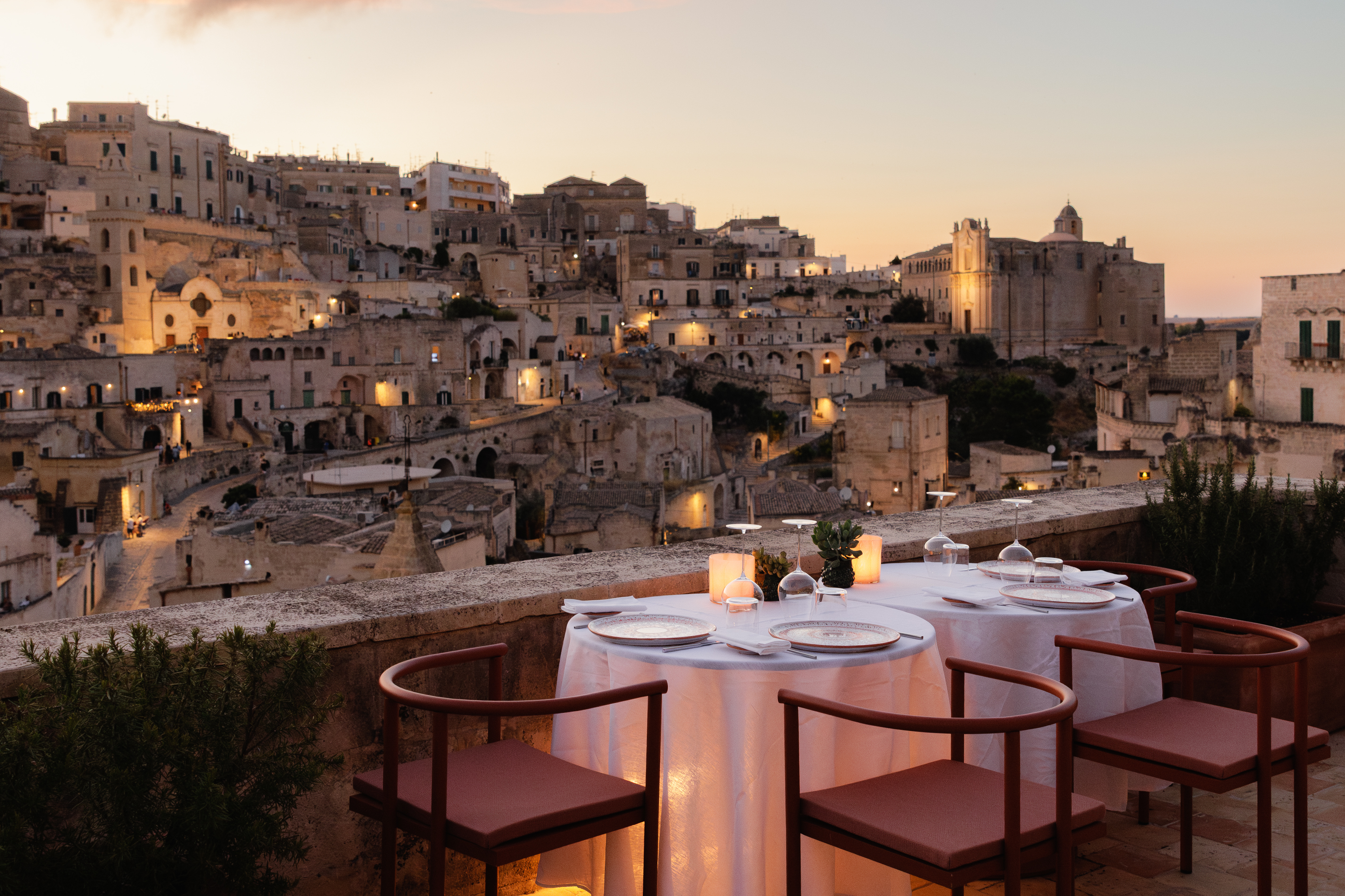 Vetera Matera balcony at sunset, with restaurant chairs and tables overlooking the hillside stone houses of Matera