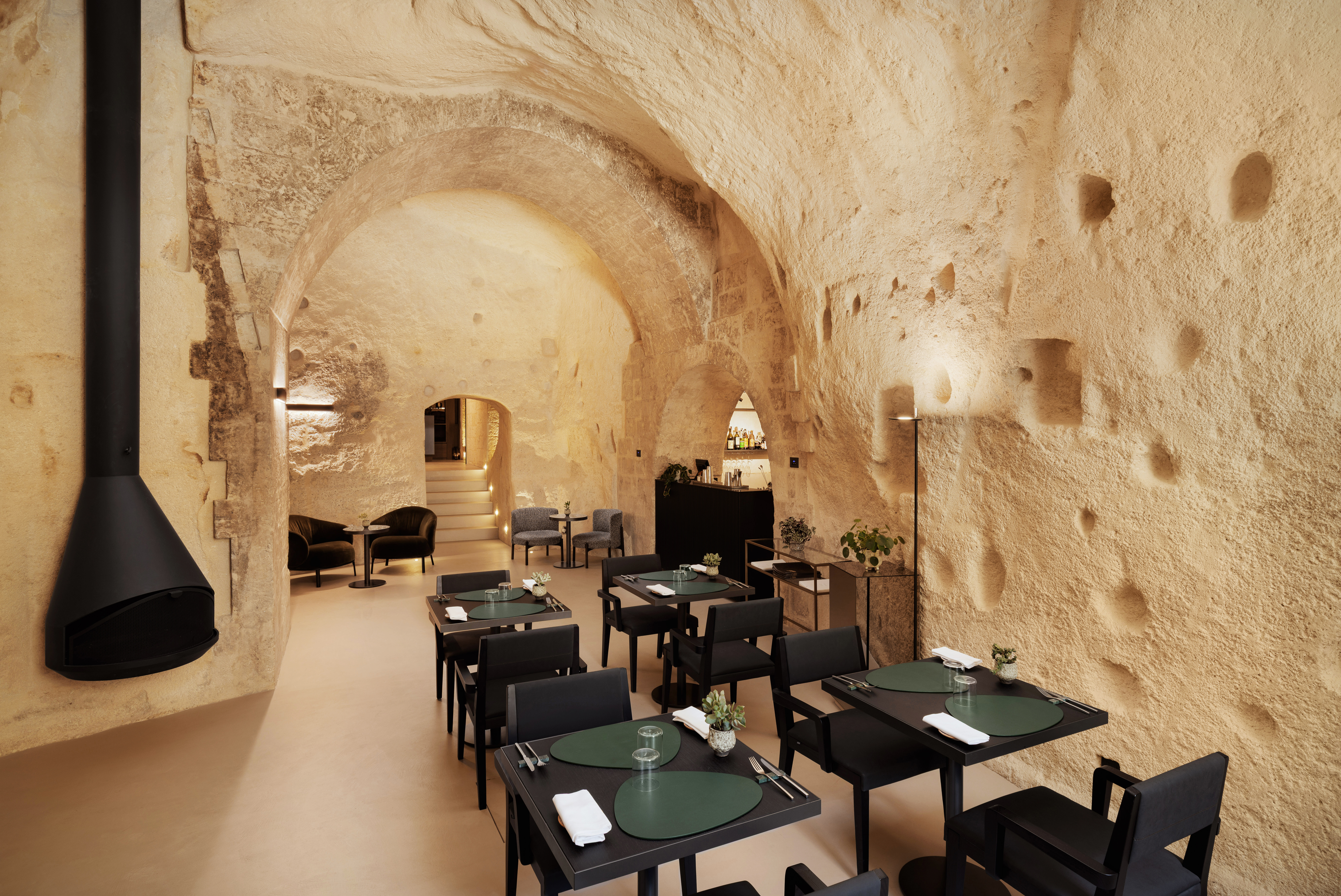 Vetera Matera bar, with black tables and chairs, modern black chimney fireplace, and curved exposed stone walls and ceiling
