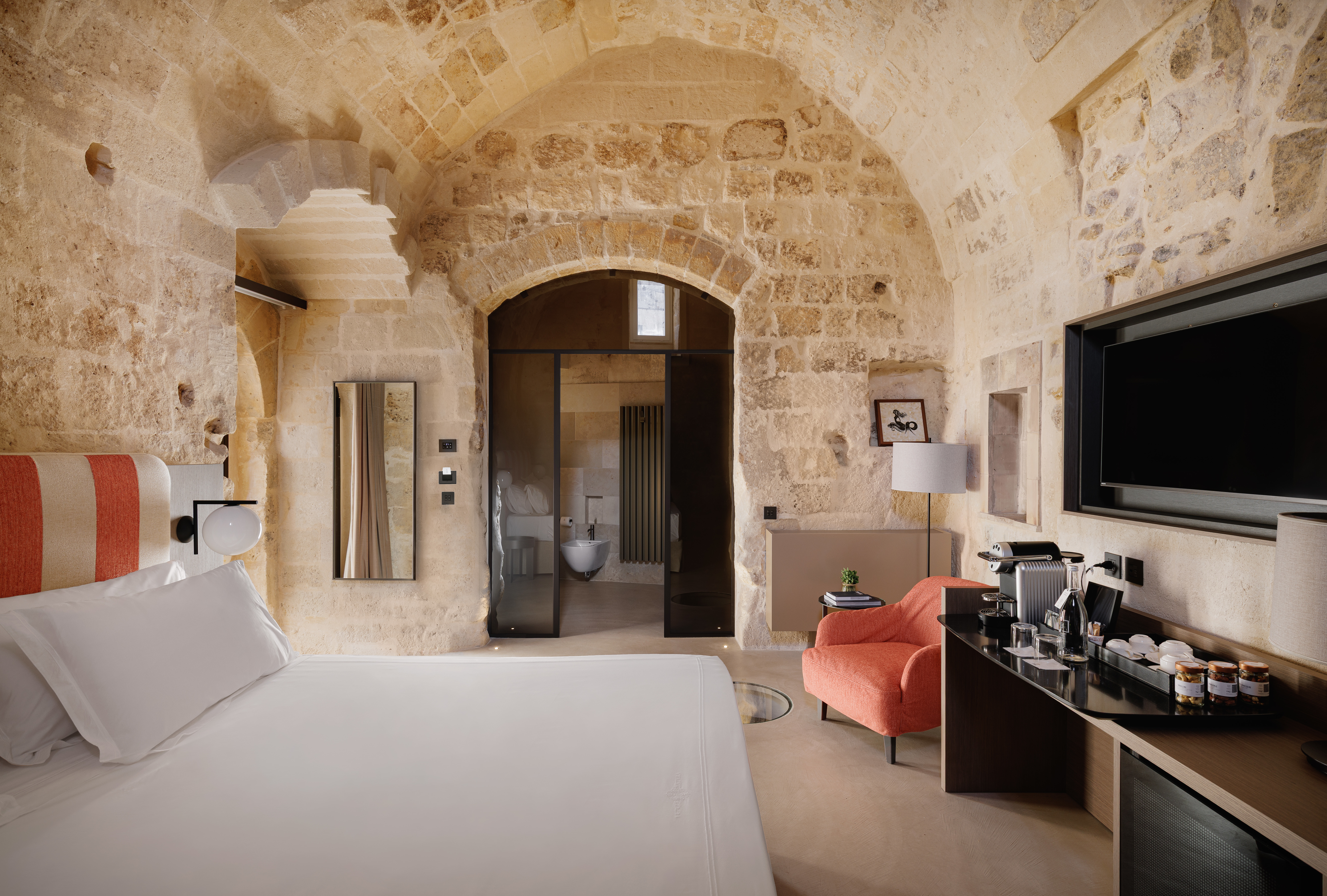 Vetera Matera hypogeal room with exposed stone walls, white bed linen, tv, and armchair, and curved ceilings