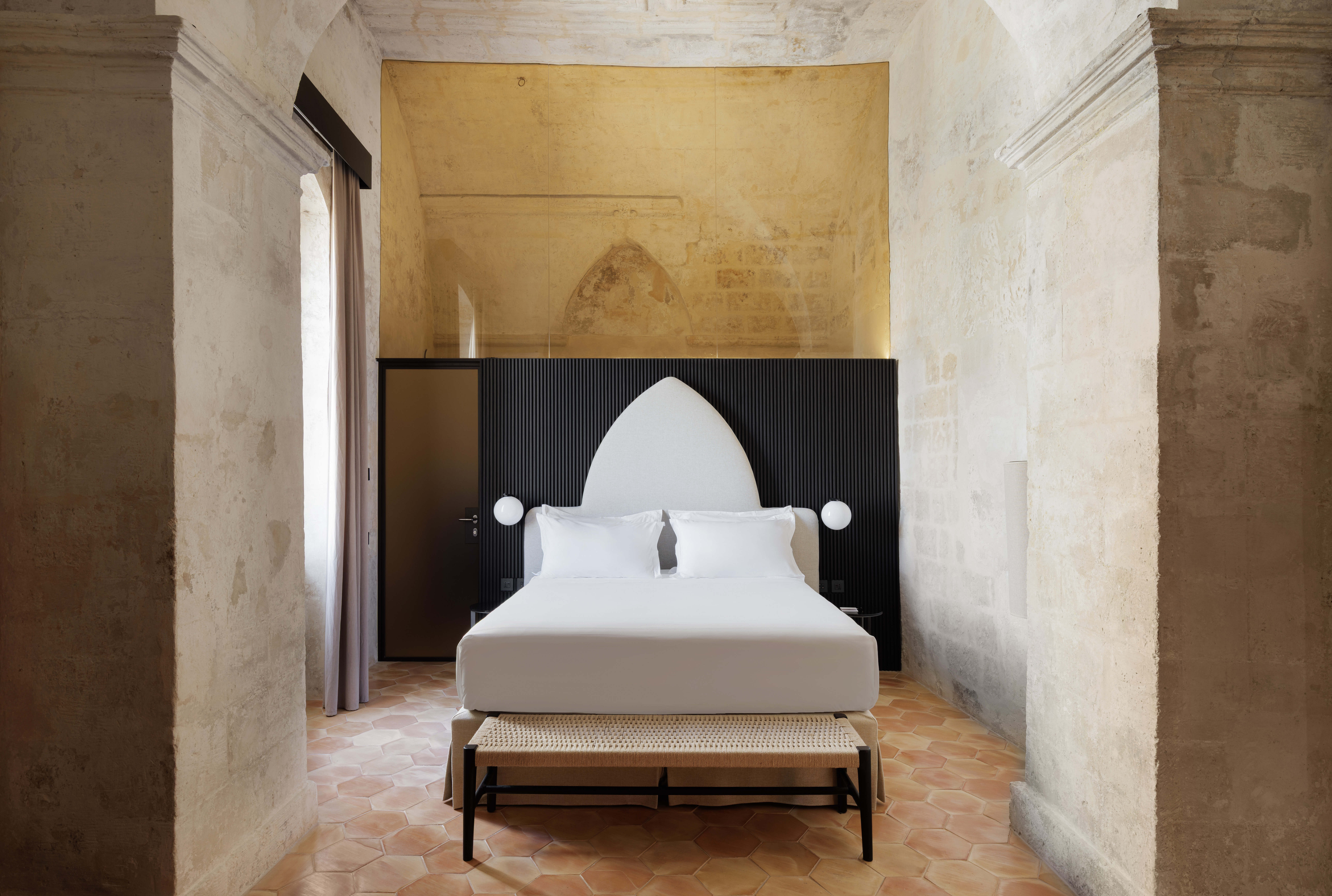 Vetera Matera hypogeal room with tall, arched ceilings, and black partition separating bedroom from bathrooms
