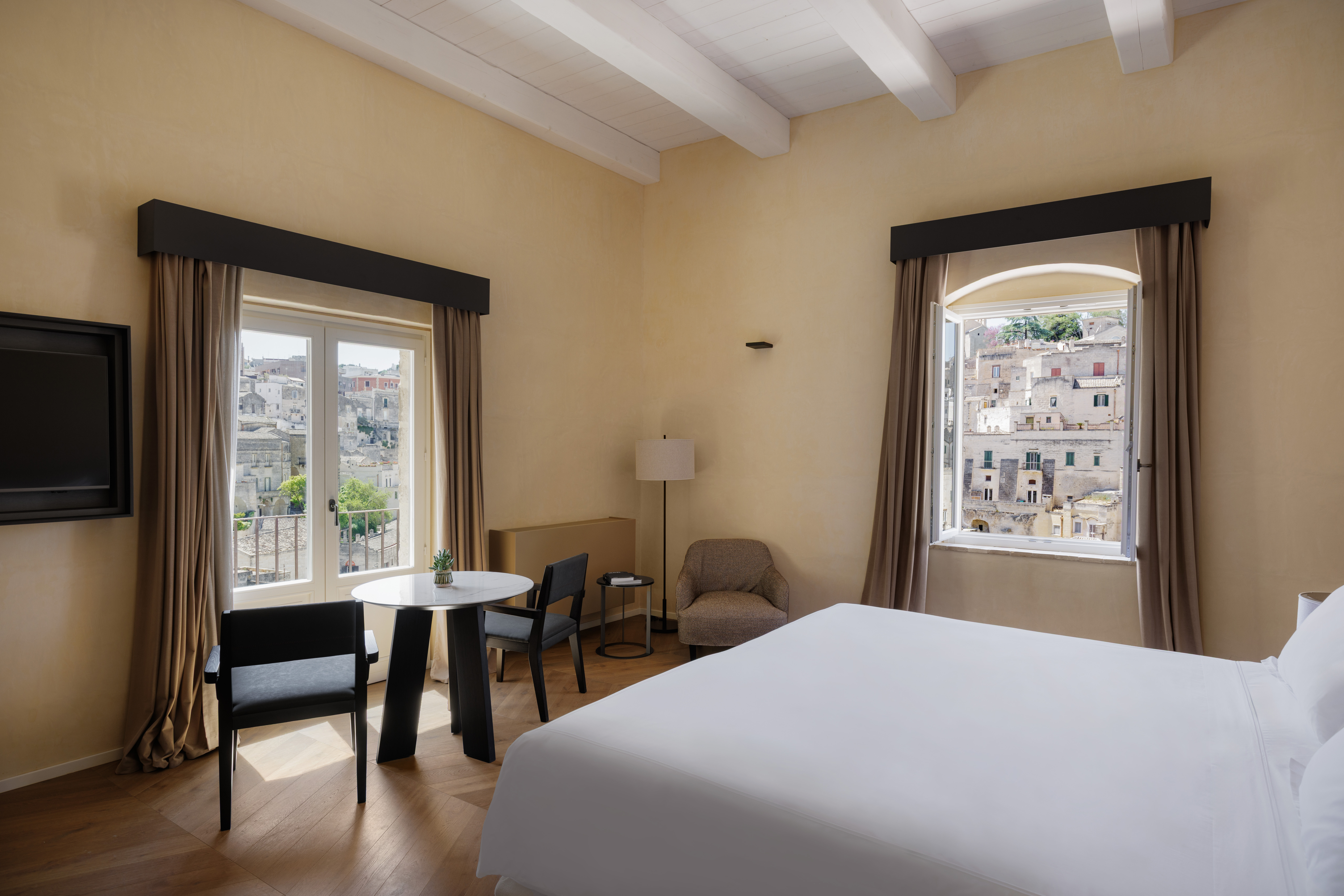 Vetera Matera Noble Floor room with white beamed ceiling, wooden floor, and large windows with town views