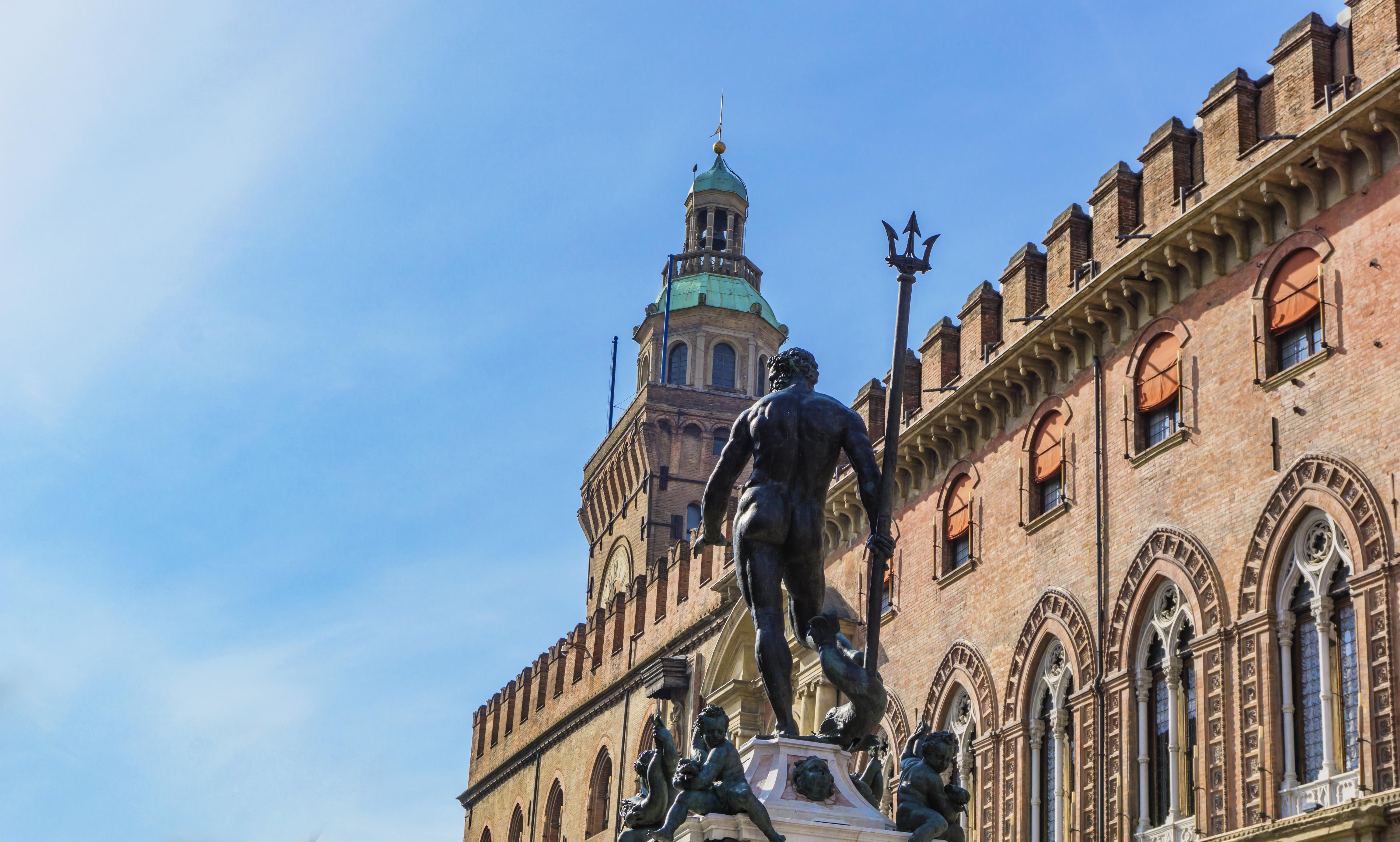 Statue of Neptune with triton outside red brick building in Bologna