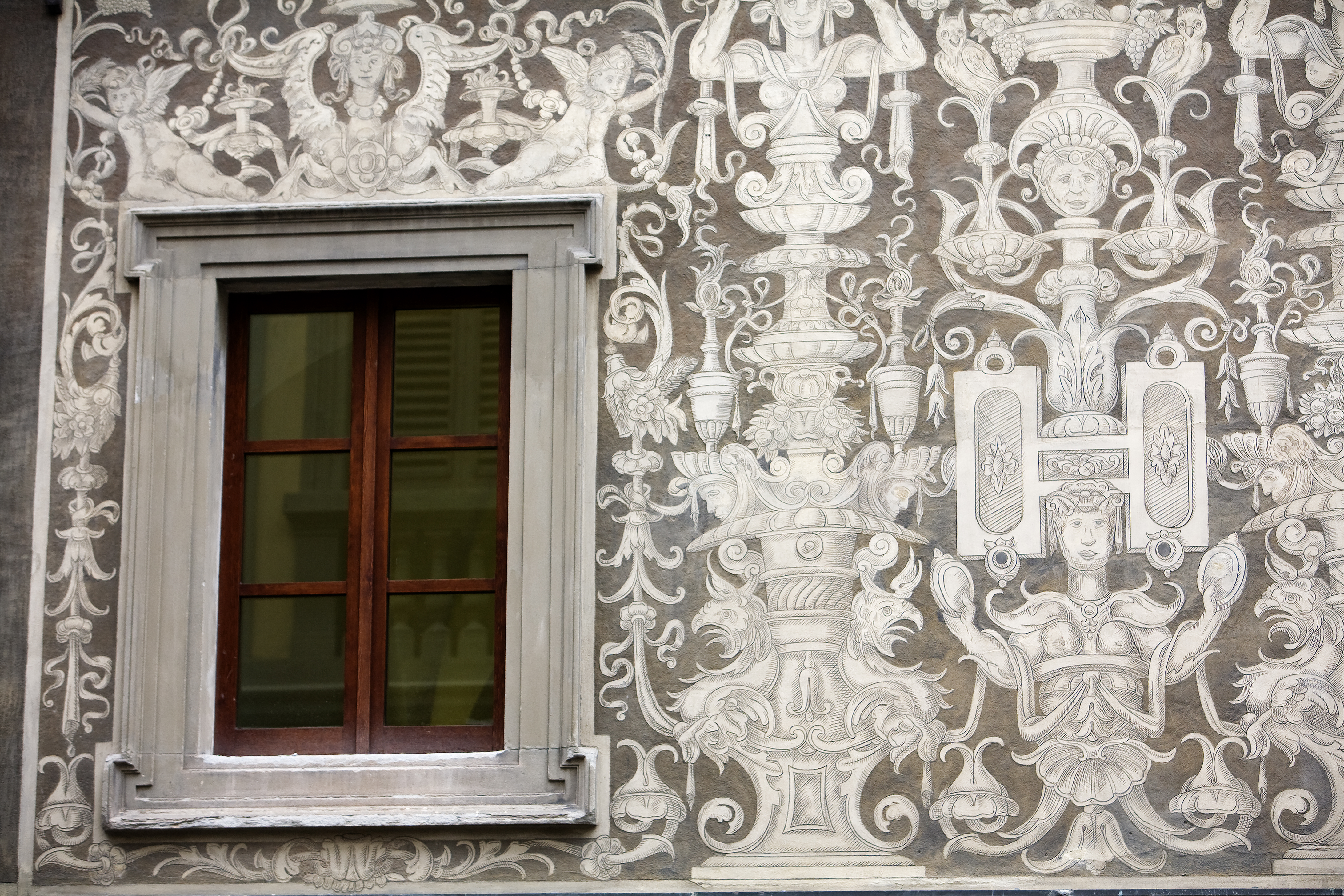 Ornate mural in white on grey stone of a wall in Florence