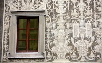Ornate mural in white on grey stone of a wall in Florence