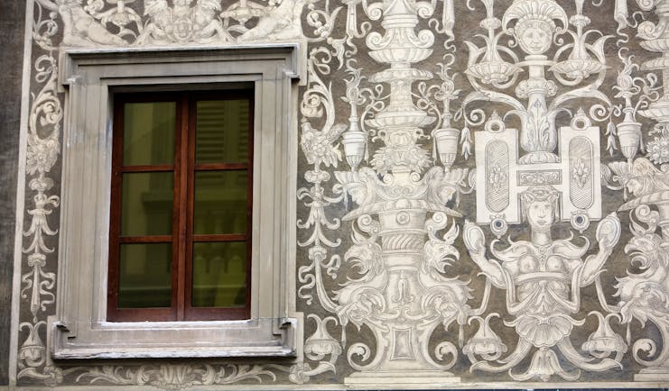 Ornate mural in white on grey stone of a wall in Florence