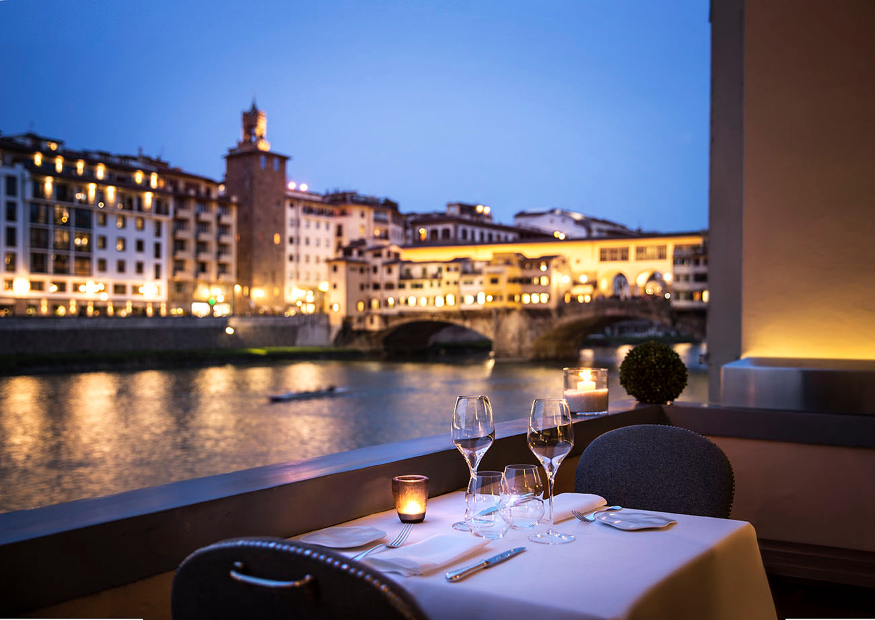 Hotel Lungarno Borgo San Jacopo Restaurant terrace, with table set for two in the evening, with the lights of the city overlooking the river beyond