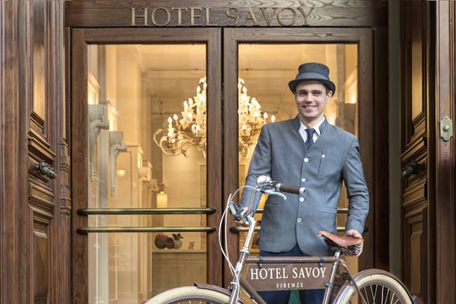 Doorman in grey with bicycle at entrance of Hotel Savoy Florence
