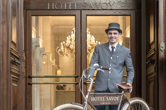 Doorman in grey with bicycle at entrance of Hotel Savoy Florence