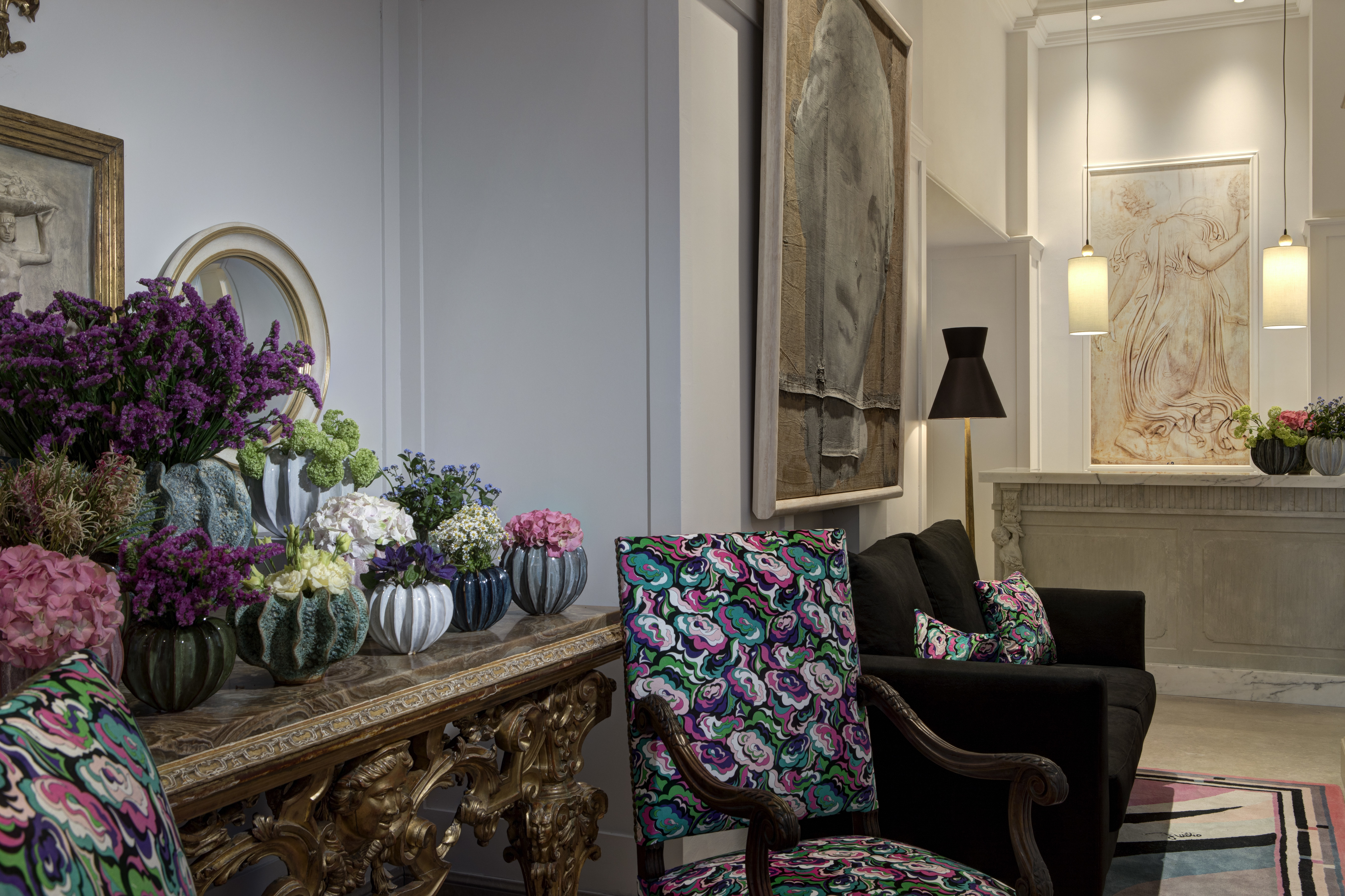 Lobby with pale walls and floors, patterned armchairs and lots of plants on a dresser at Hotel Savoy Florence