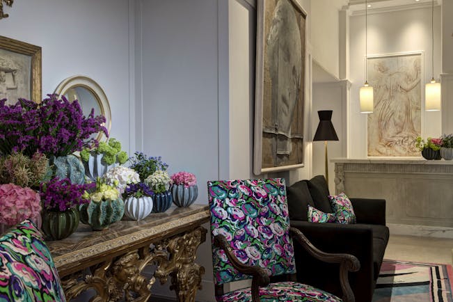 Lobby with pale walls and floors, patterned armchairs and lots of plants on a dresser at Hotel Savoy Florence