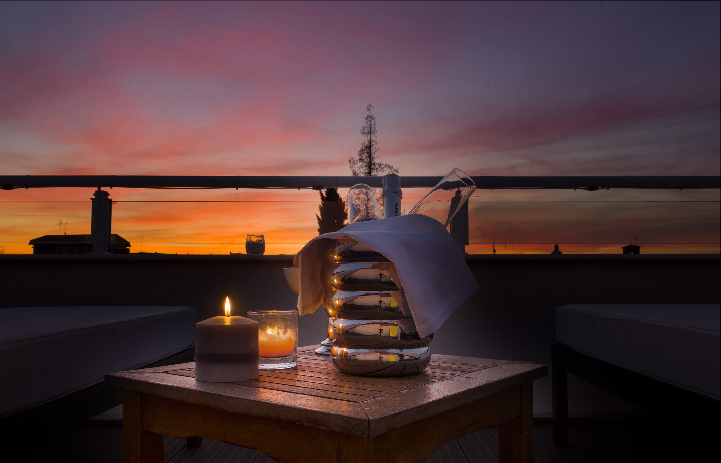 Hotel Palazzo Bezzi rooftop at night, with a bottle of champagne on a candlelit table for two, looking out of the silhouetted rooftops of the city