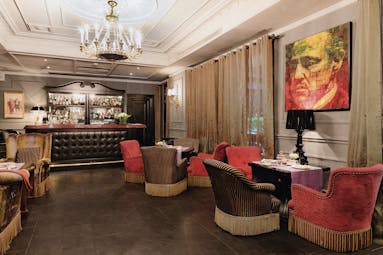 Bar and cafe at the Baglioni Hotel Carlton, with red and brown arm chairs placed around the wooden floors with a bar at the back of the room